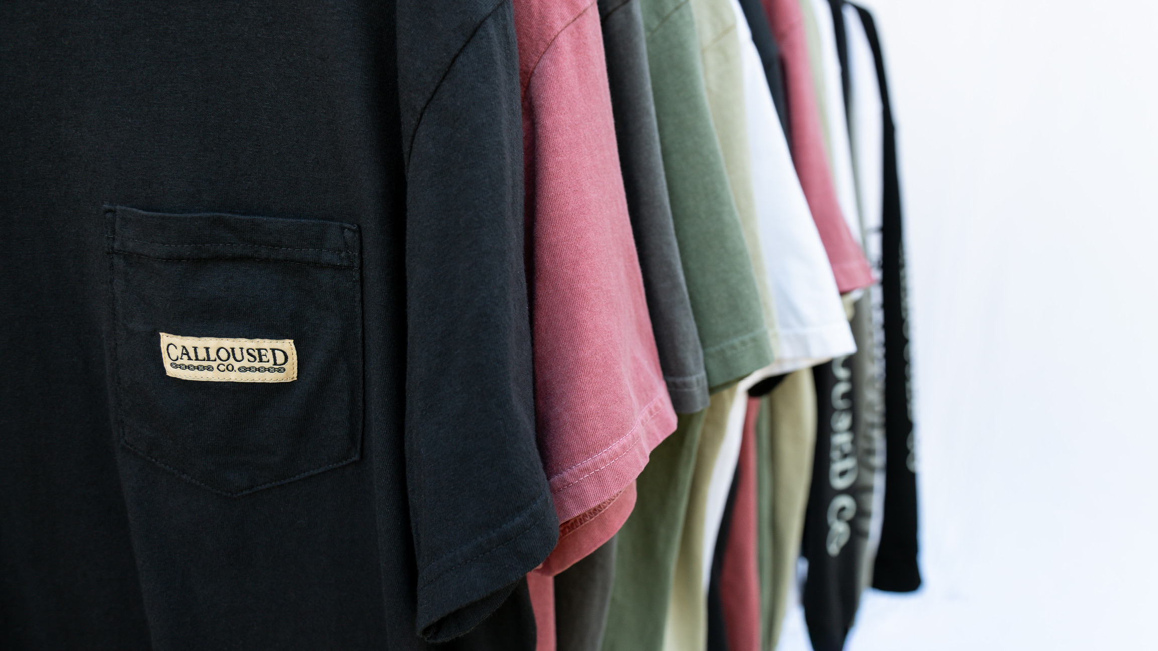 Row of folded shirts with visible 'Calloused Co' brand label on a white background.