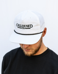 Person wearing a white cap with 'Calloused Co.' logo on a plain background