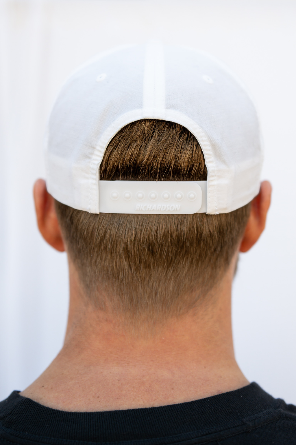 Person wearing a white cap from behind on a plain background