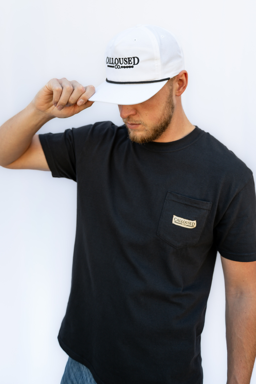Man wearing a black t-shirt with 'Calloused Co' logo and a white cap with text, against a white background