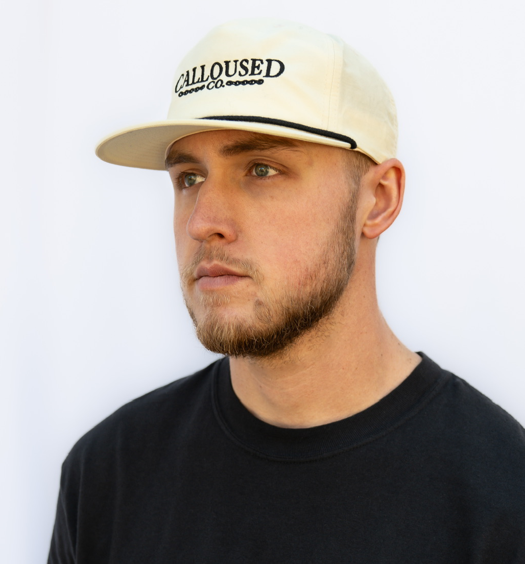 Man wearing a beige/birch cap with 'Calloused Co' logo against a white background