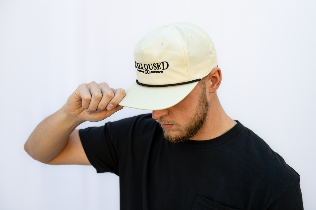 Person wearing a beige/birch cap with 'Calloused Co' logo on a white background