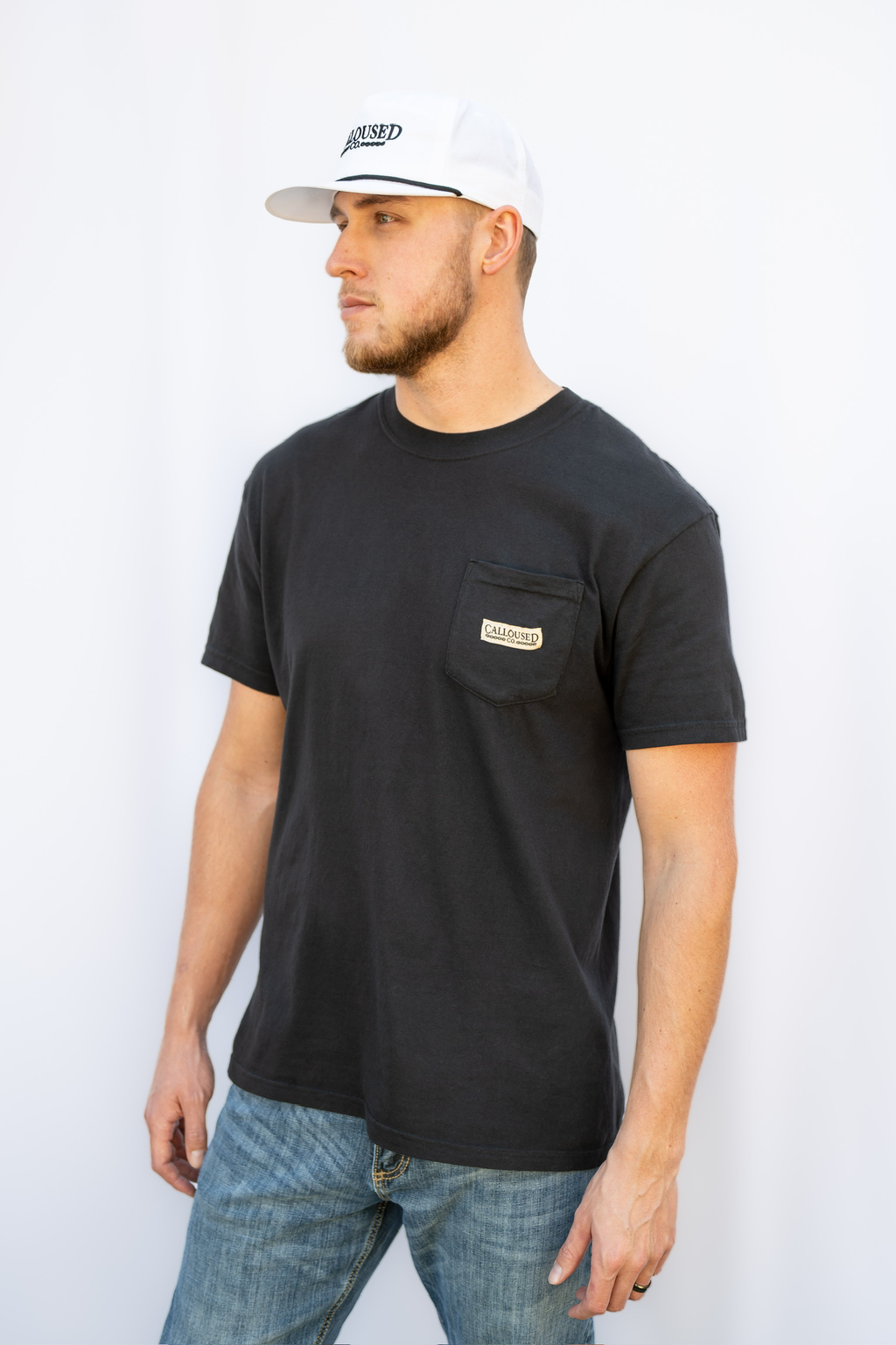 Man wearing a black t-shirt with 'Calloused Co' branding on the pocket and a white cap against a white background