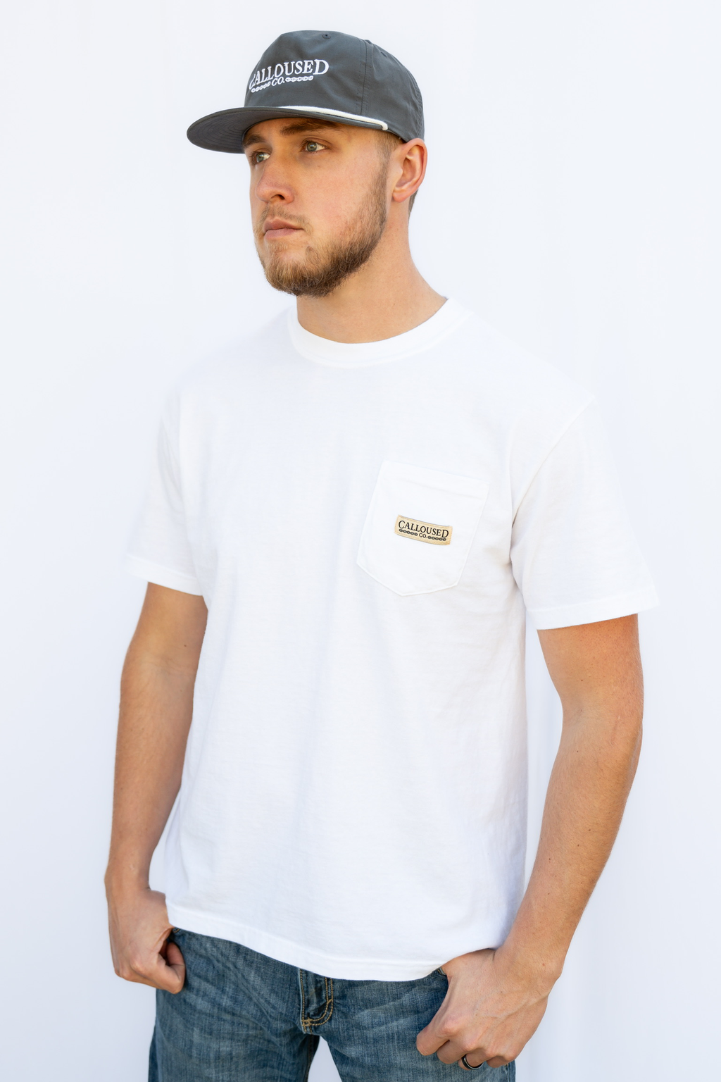 Man wearing a white t-shirt with 'Calloused Co' logo and a gray cap on a white background