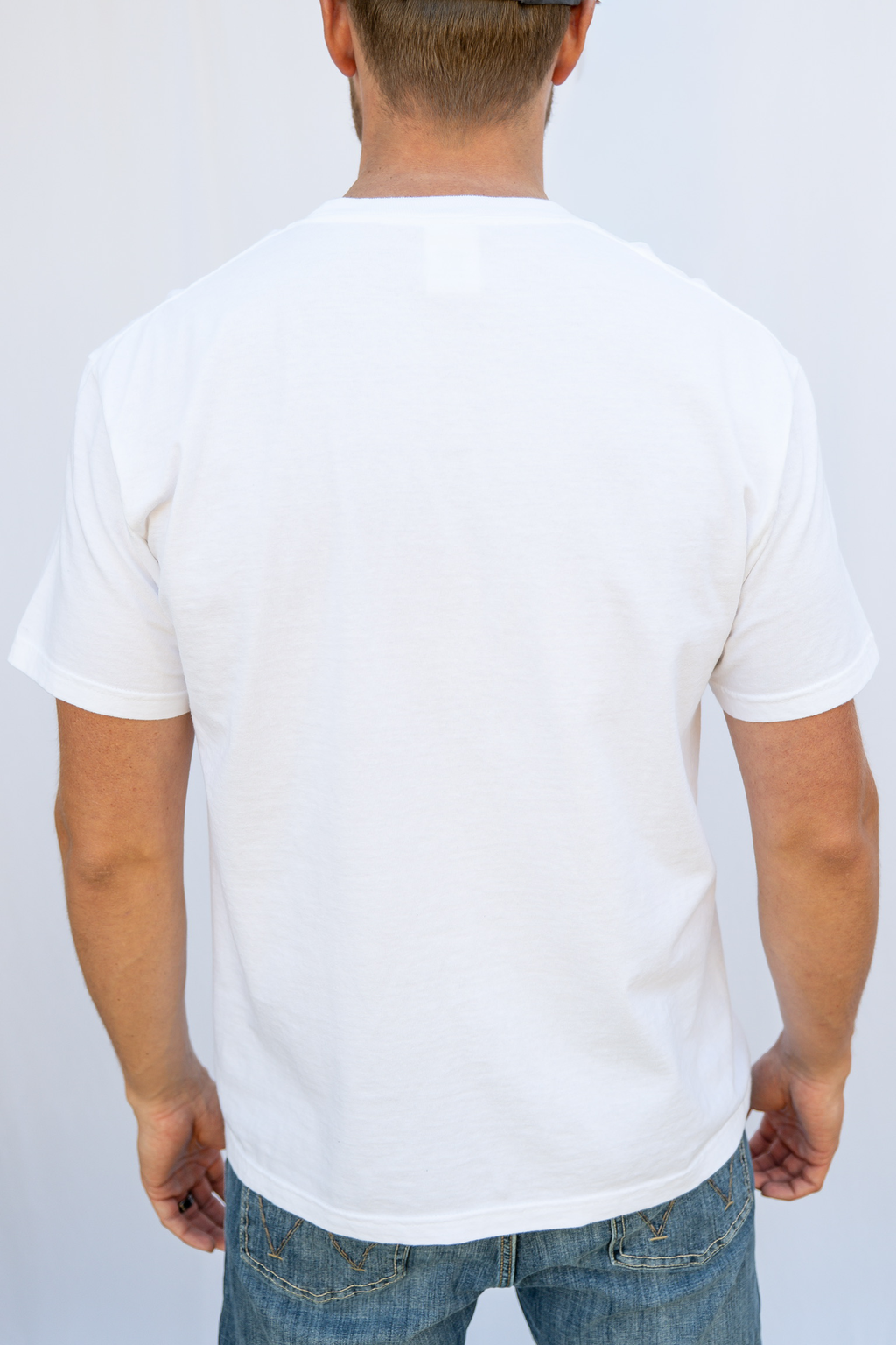 Person wearing a plain white t-shirt and blue jeans on a light gray background
