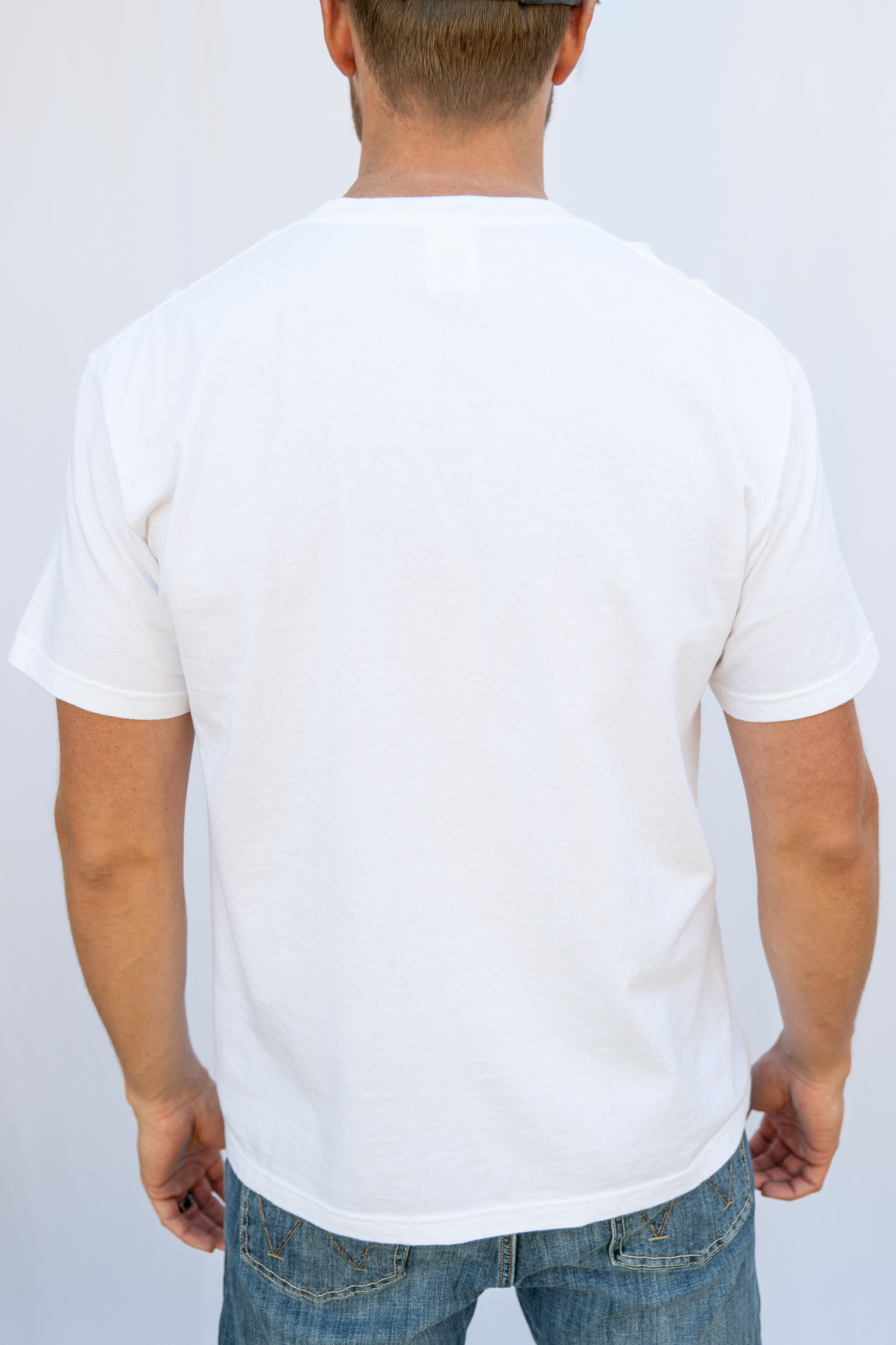 Person wearing a plain white t-shirt and blue jeans on a light gray background
