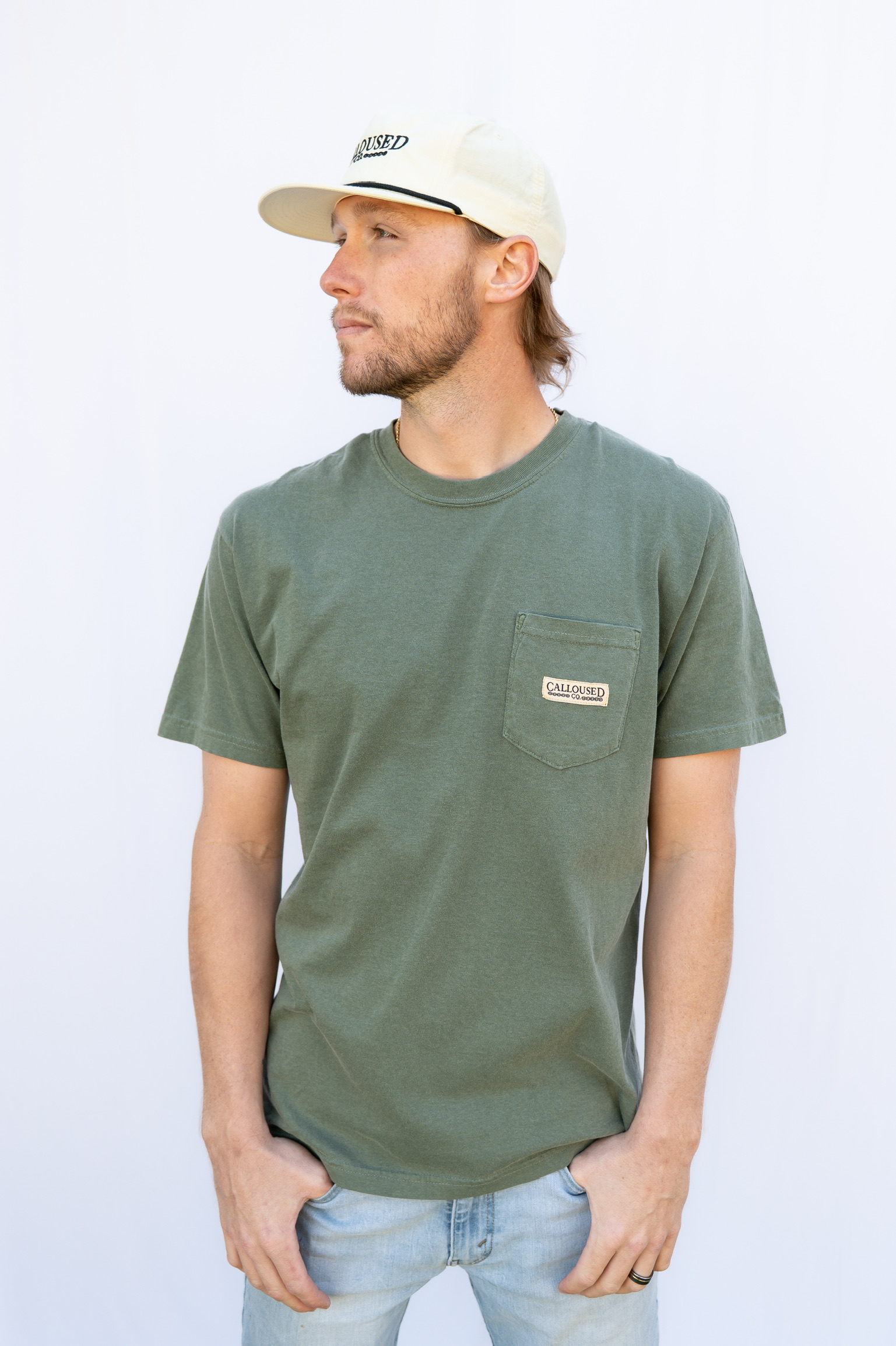 Man wearing a green t-shirt with 'Calloused Co' logo and a beige cap on a light gray background
