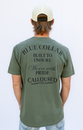 Person wearing a moss green t-shirt with 'Blue Collar Built to Endure Worn with Pride' text, 'Calloused Co' logo on the back, standing against a white background