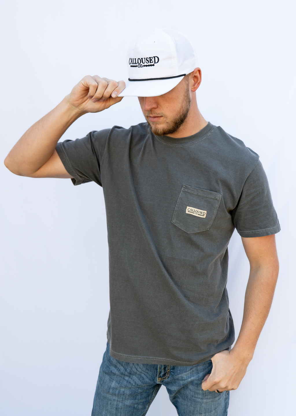 Man wearing a gray t-shirt with a pocket and a white cap with 'Calloused Co' logo, against a light blue background