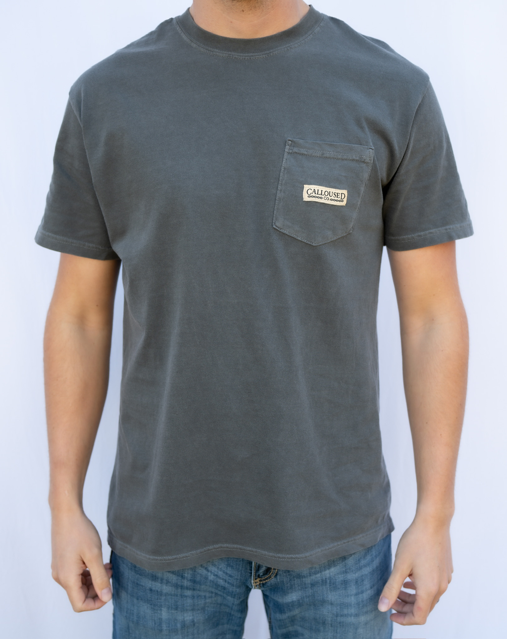 Person wearing a gray t-shirt with a pocket and visible 'Calloused Co' brand logo on a white background
