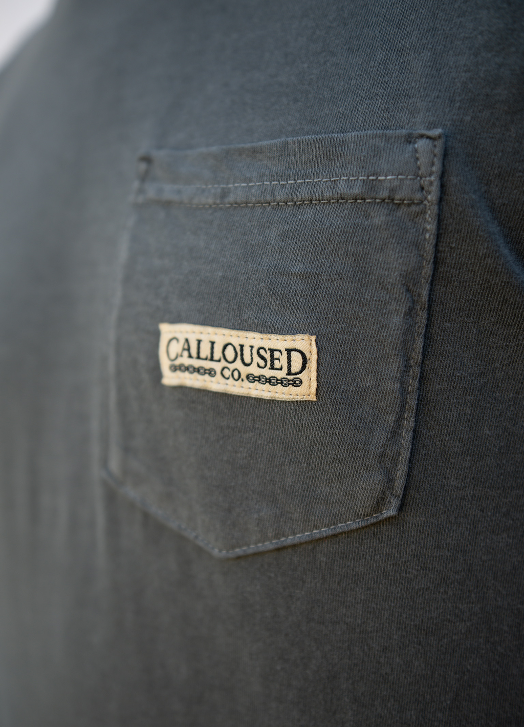 Close-up of a dark gray shirt with a 'Calloused Co' logo on the chest pocket.