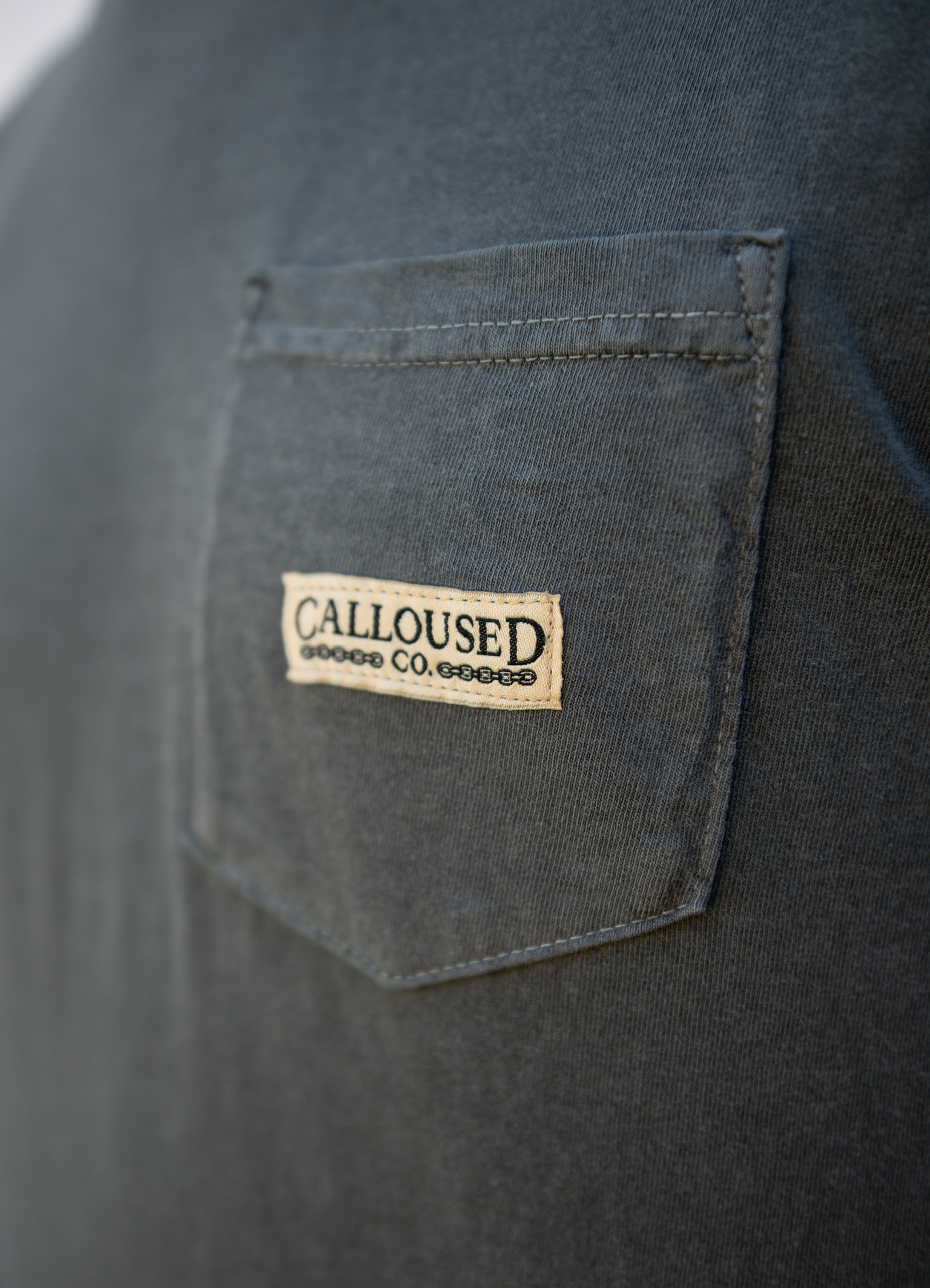 Close-up of a dark gray shirt with a 'Calloused Co' logo on the chest pocket.