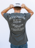 Person wearing a gray t-shirt with 'Blue Collar Built to Endure Worn with Pride' text, 'Calloused Co' logo, and a white cap, on a plain background