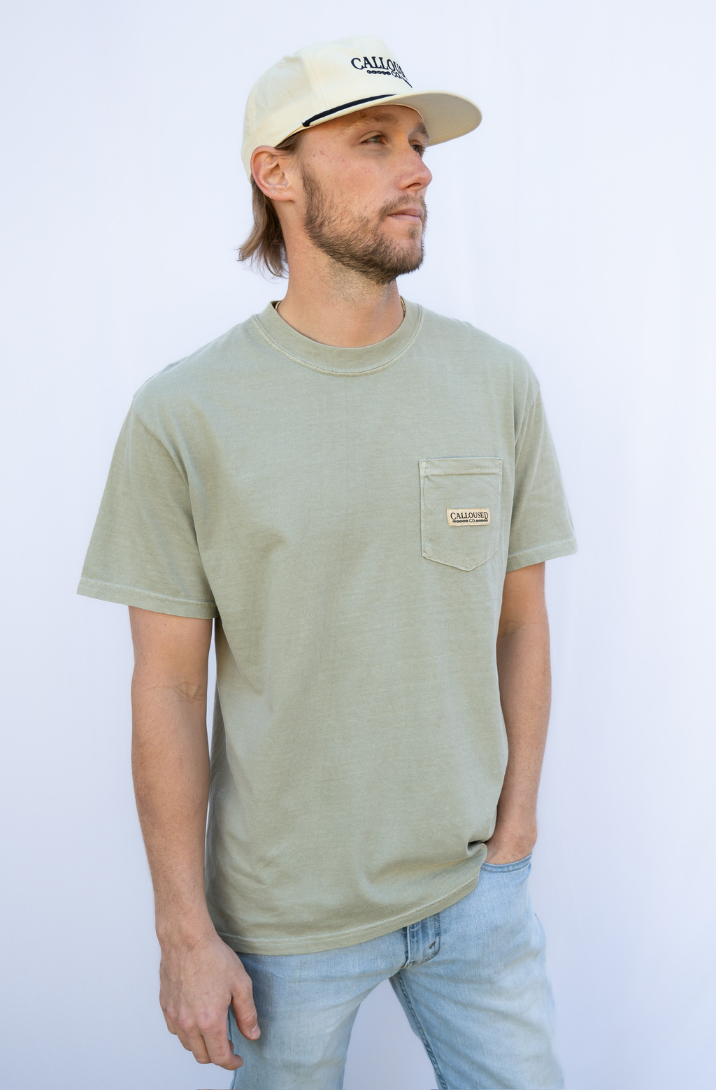 Man wearing a 'Calloused Co' sandstone t-shirt and beige cap against a white background
