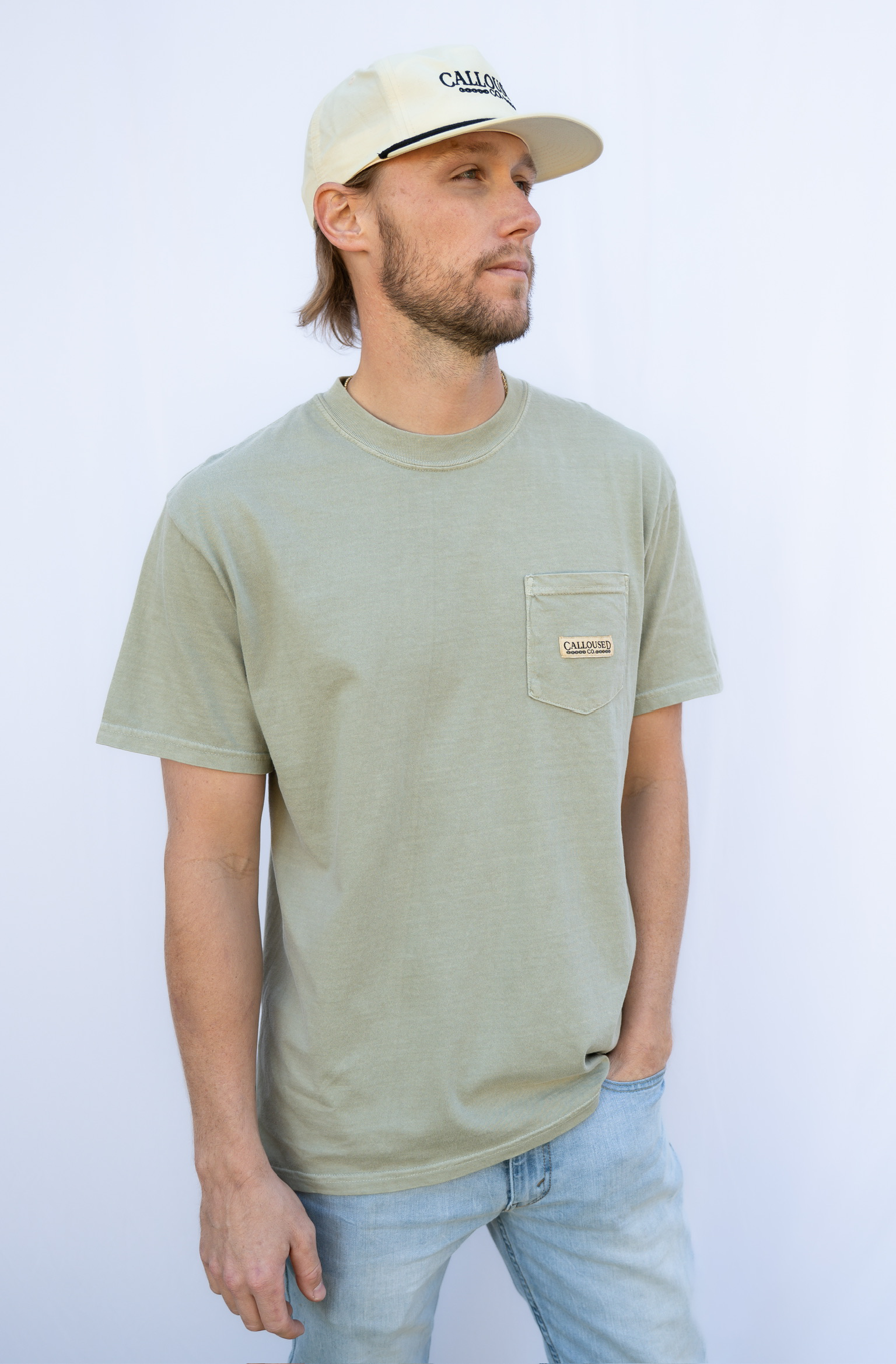 Man wearing a sandstone 'Calloused Co' t-shirt and beige cap against a white background.