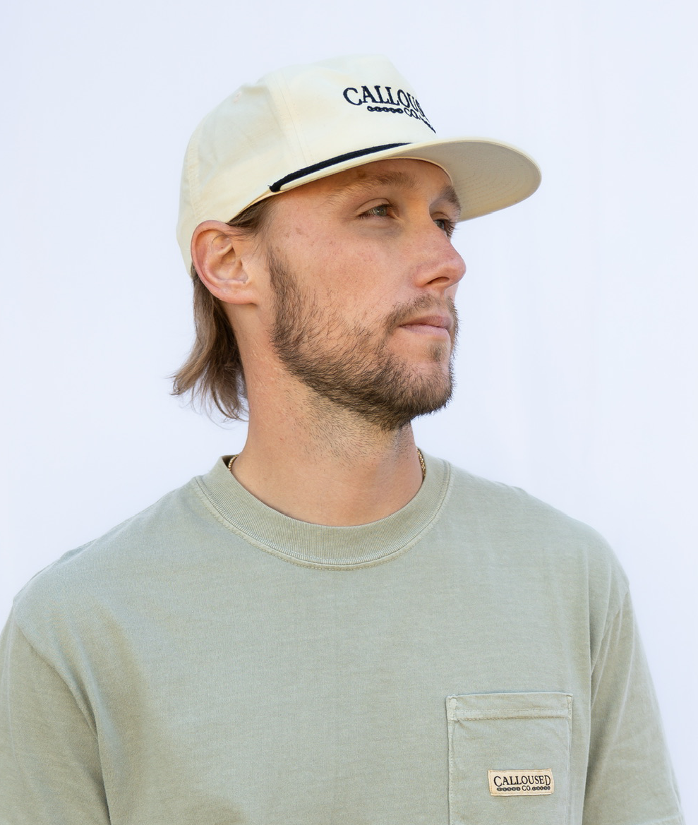 Man wearing a beige/birch cap and shirt with 'Calloused Co' branding on a light background