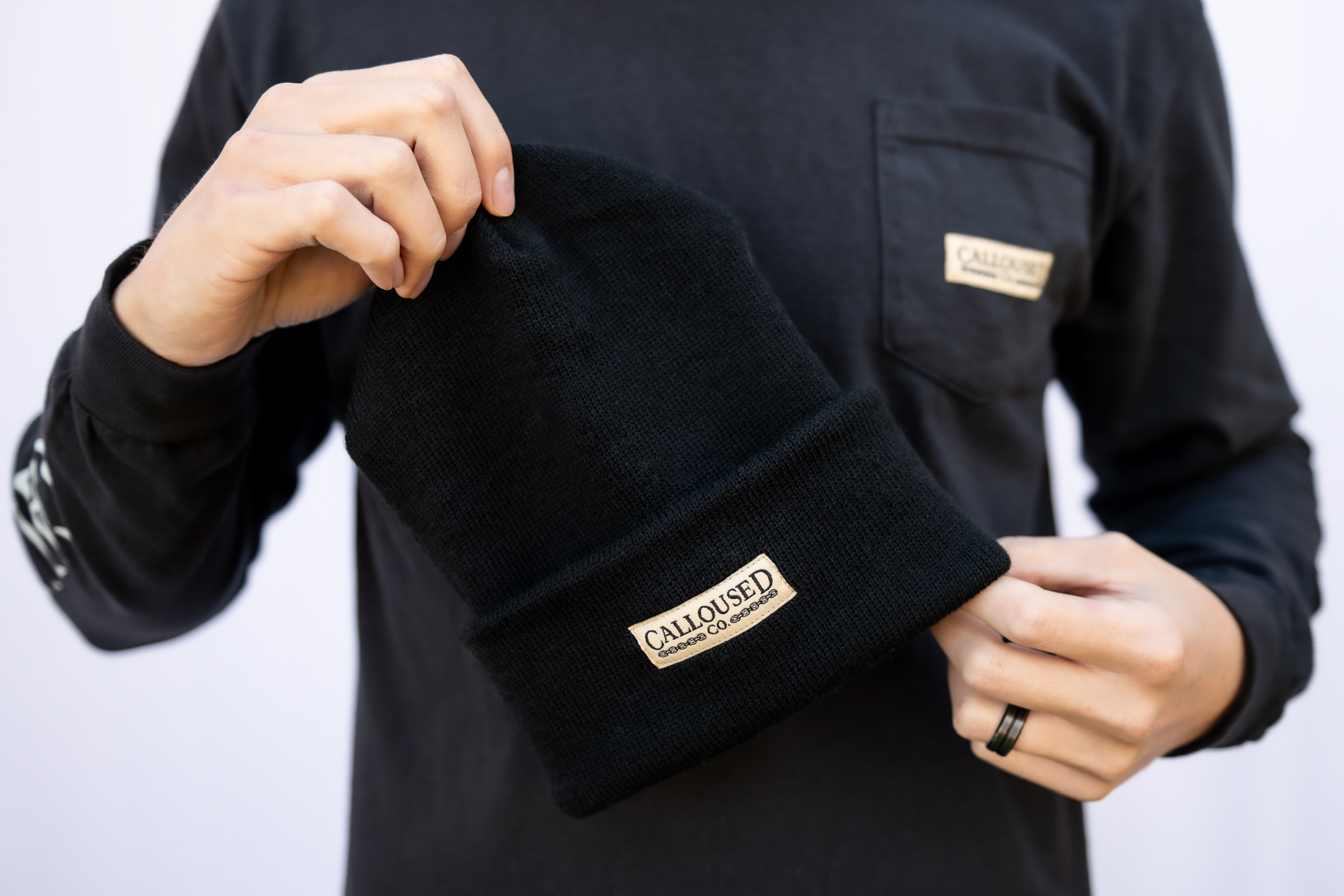 Person holding a black beanie with 'Calloused Co' brand logo against a white background