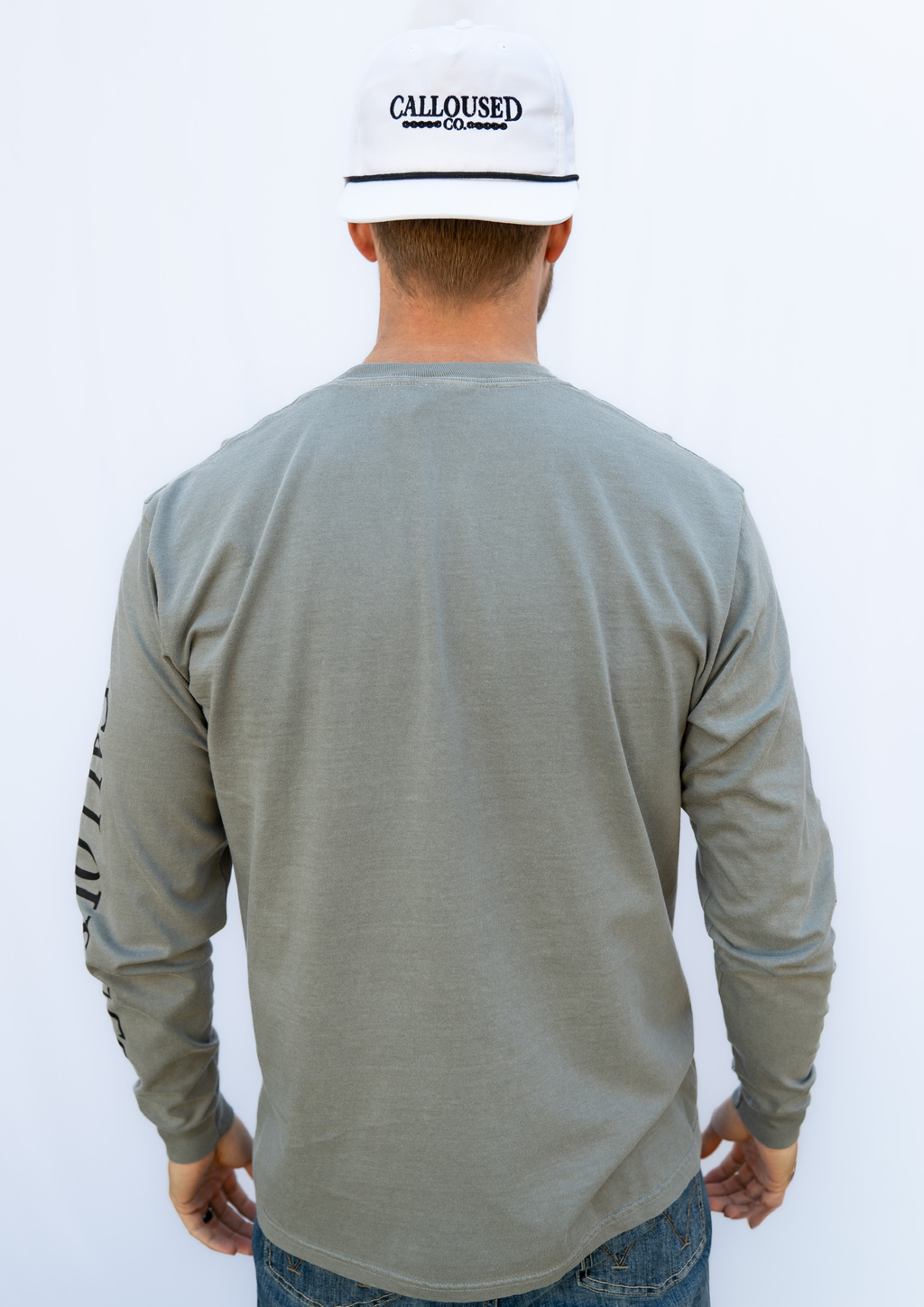 Person wearing a gray long-sleeve shirt and white cap with 'Calloused Co' logo on a white background