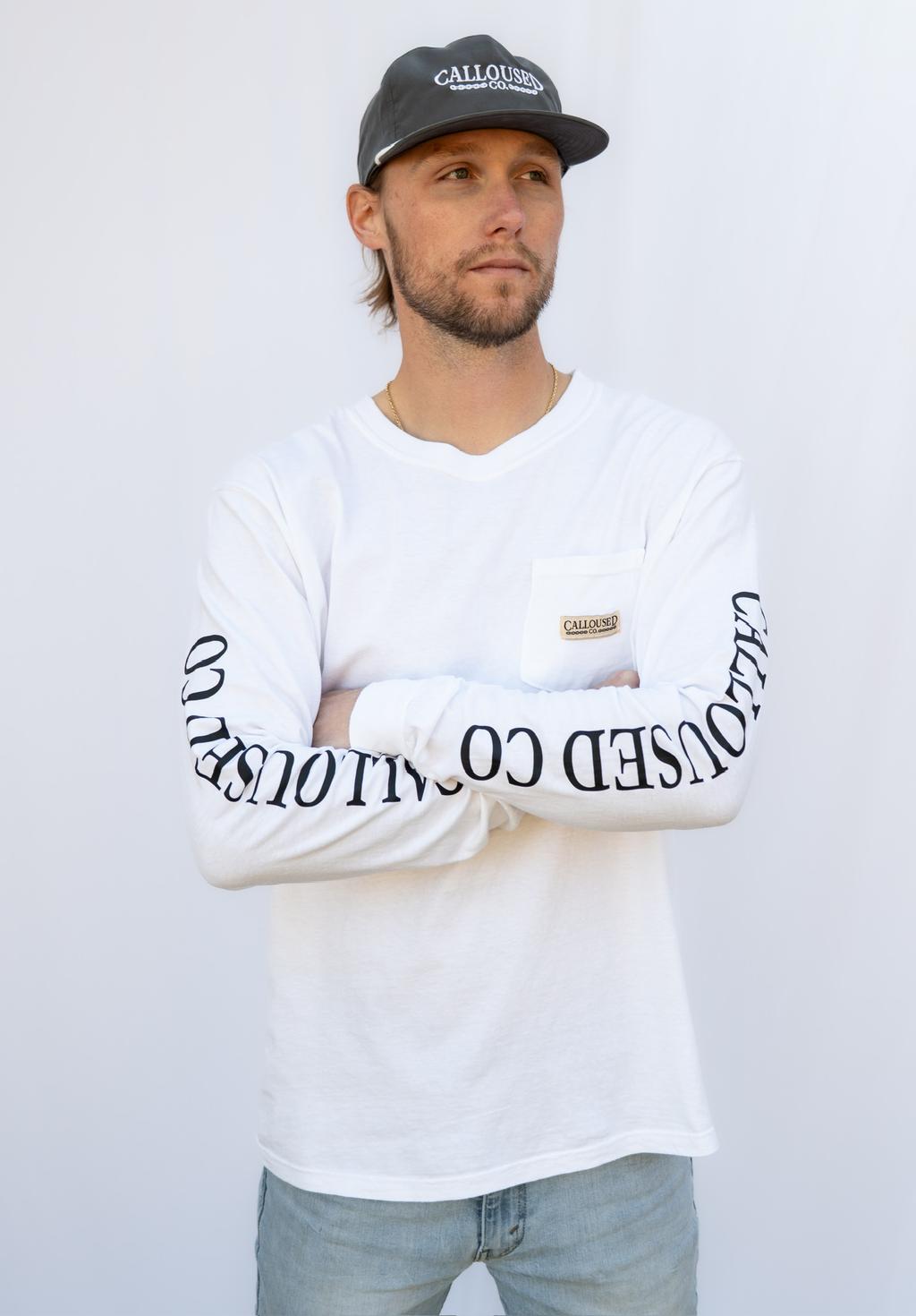 Man wearing a white long-sleeve shirt with 'Calloused Co' text and a black cap on a white background