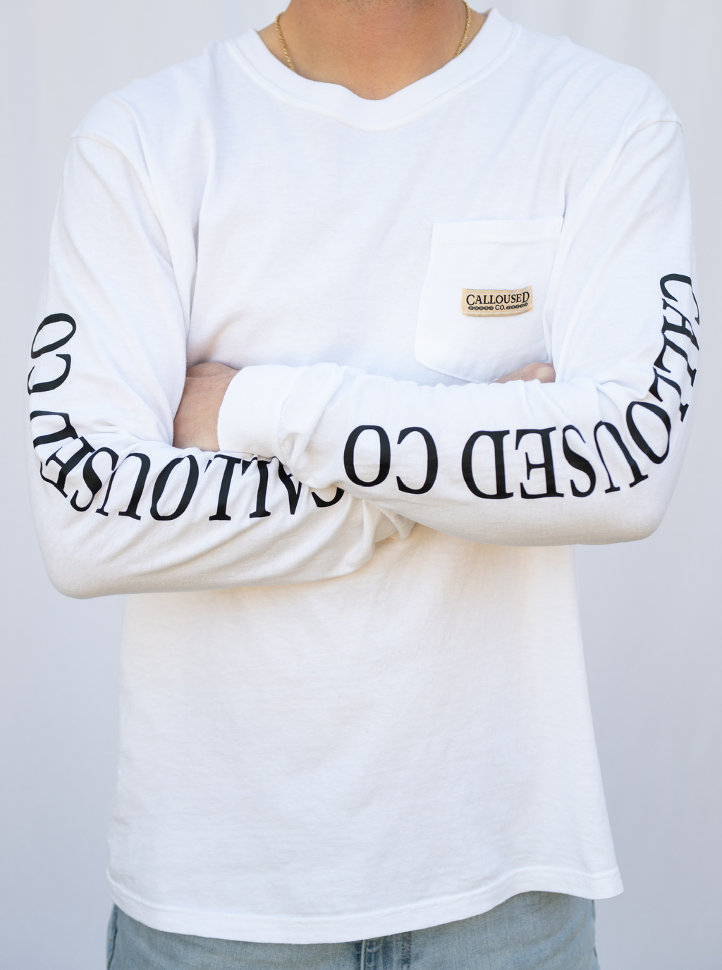 Person wearing a white long-sleeve shirt with 'Calloused Co' text on sleeves against a plain background