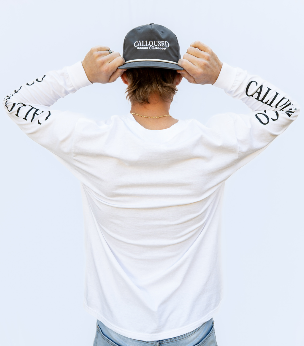 Person wearing a white long-sleeve shirt with 'Calloused Co' branding and a gray cap.